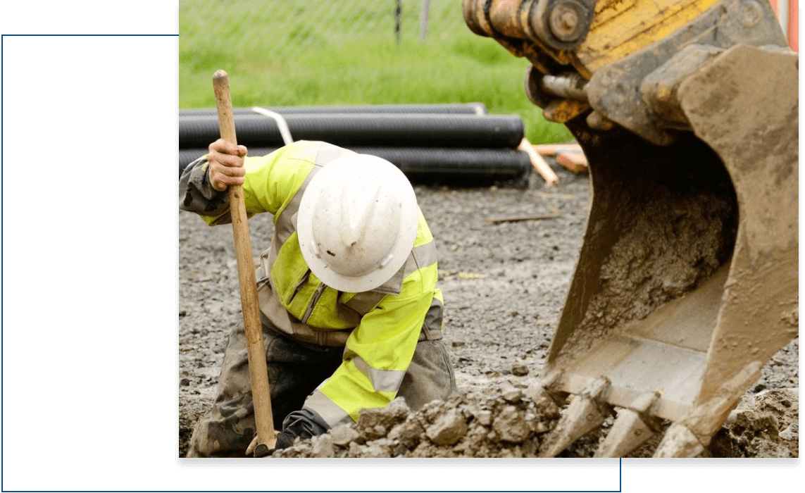 A man in yellow jacket digging with shovel.