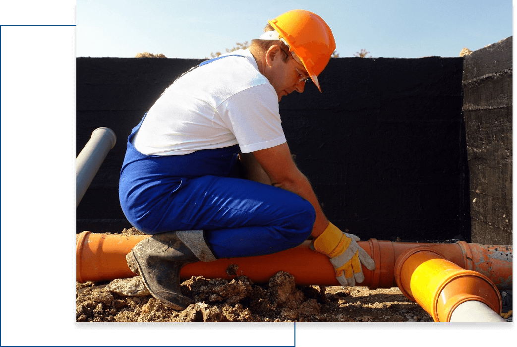 A man kneeling down on the ground next to pipes.